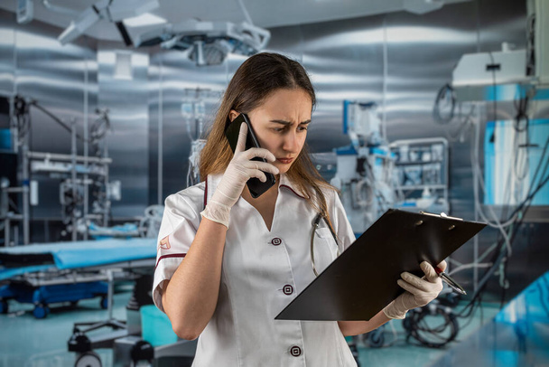 Mooie vrouw dokter draagt witte jas uniform lezen patiënt informatie in operatiekamer. Gezondheidszorgconcept - Foto, afbeelding