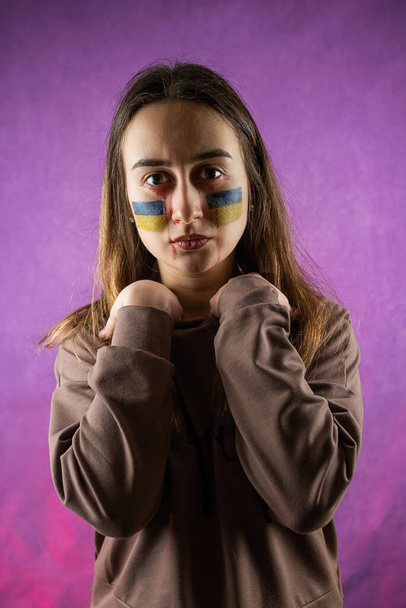 Vrij jonge bange vrouw met Oekraïense vlag op gezicht geïsoleerd op dard achtergrond. Concept vrede. Bid voor Oekraïne - Foto, afbeelding