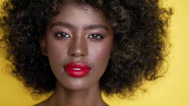 Очаровательная афроамериканка с вьющимися волосами смотрит в камеру, стоя на жёлтом фоне. - Кадры, видео