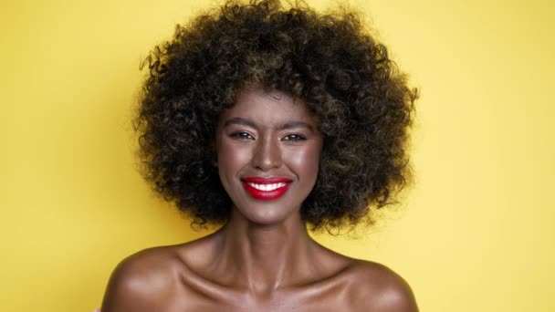 Mulher afro-americana otimista com cabelo encaracolado sorrindo e olhando para a câmera contra fundo amarelo - Filmagem, Vídeo