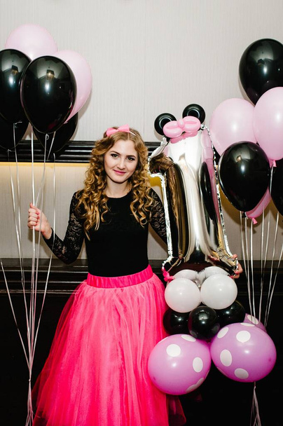 Beautiful woman in luxury lush princess in pink dresses with tulle. Fashion lady in gorgeous long gown posing isolated on balloons background. Concept of birthday celebration daughter is 1 year. - Foto, Imagem