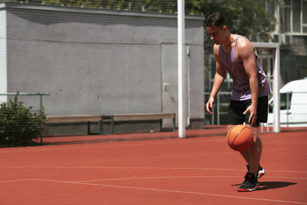 young guy plays basketball on the basketball court. throws the ball into the ring. doing sports. healthy body and healthy lifestyle - Foto, afbeelding