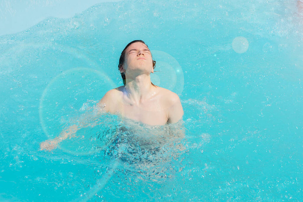 мокрый парень выпрыгивает из воды бассейна с закрытыми глазами на солнце, мужчина купает меня в бассейне в летний день, частный отдых. - Фото, изображение