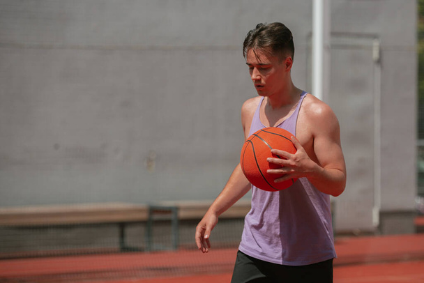 young guy plays basketball on the basketball court. throws the ball into the ring. doing sports. healthy body and healthy lifestyle - Photo, Image