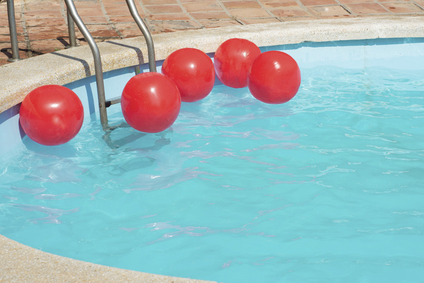 bolas inflables rojas brillantes flotan en la superficie del agua del laurel en la piscina en el sol. - Foto, Imagen