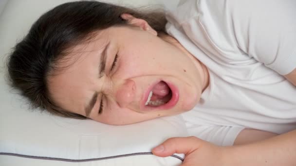 Eine 30-jährige brünette Frau gähnt auf einem Kissen auf ihrem Bett liegend. - Filmmaterial, Video