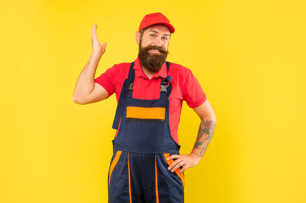 smiling funny bearded man technician in work clothes on yellow background. - Fotó, kép