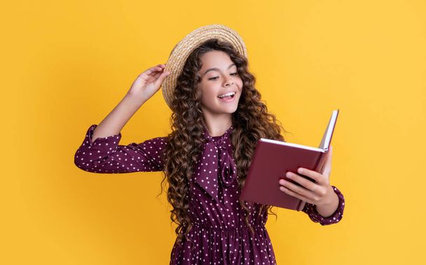 happy child with frizz hair recite book on yellow background. - Zdjęcie, obraz