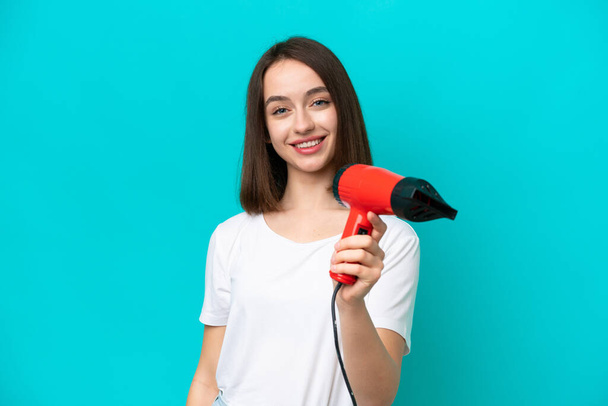 Young Ukrainian holding a hairdryer isolated on blue background with happy expression - Photo, Image
