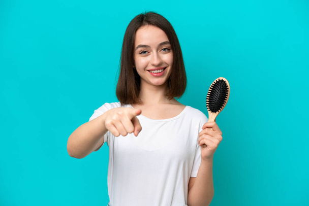 Young ukrainian woman with hair comb isolated on blue background points finger at you with a confident expression - 写真・画像