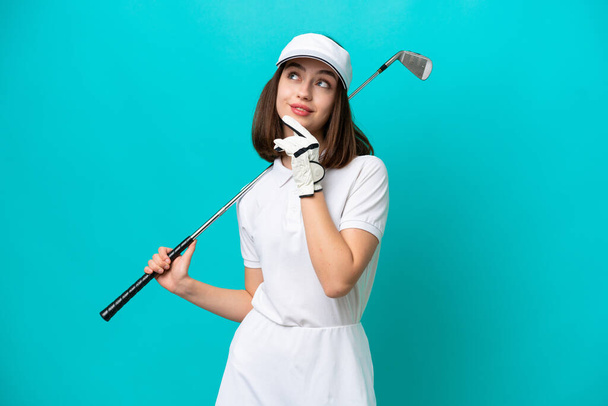Young Ukrainian golfer player woman isolated on blue background and looking up - Fotografie, Obrázek