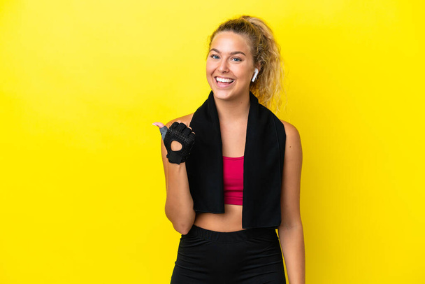 Sport woman with towel isolated on yellow background pointing to the side to present a product - Photo, Image