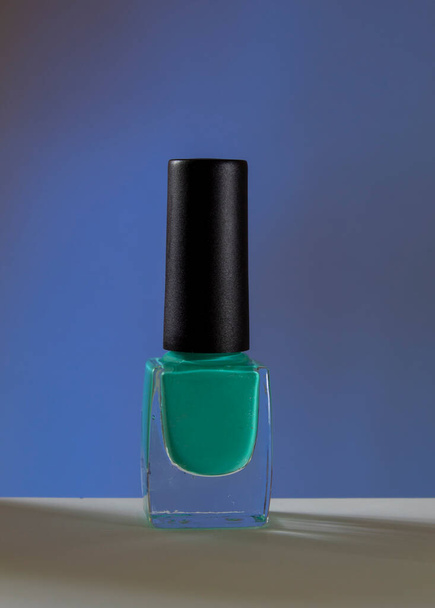 In the foreground, a transparent bottle with turquoise nail polish close-up. The background is blue. Beauty and nail care woman. - Photo, image