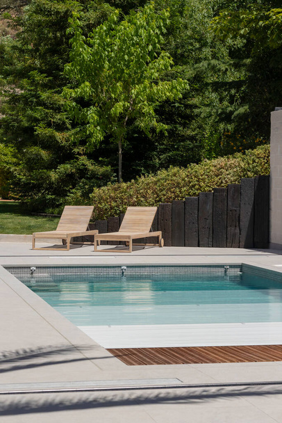 Pionowy widok na basen w ogrodzie domu z drewnianymi leżakami i roletą basenową w lecie - Zdjęcie, obraz
