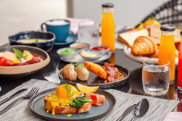 Delicious breakfast in luxury hotel. Table with plates full of various fresh food in cafe, freshly squeezed juices, eggs, fruits and sausages. Morning buffet food in front in modern resort. - Fotó, kép