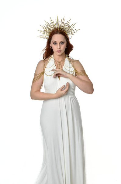 retrato de mujer hermosa cabeza roja con vestido de toga de fantasía de flujo largo con corona halo de oro angelical en el fondo del estudio - Foto, Imagen
