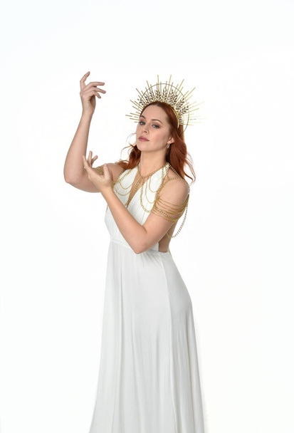 retrato de mujer hermosa cabeza roja con vestido de toga de fantasía de flujo largo con corona halo de oro angelical en el fondo del estudio - Foto, imagen