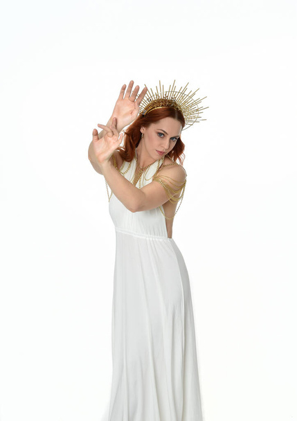 retrato de mujer hermosa cabeza roja con vestido de toga de fantasía de flujo largo con corona halo de oro angelical en el fondo del estudio - Foto, imagen