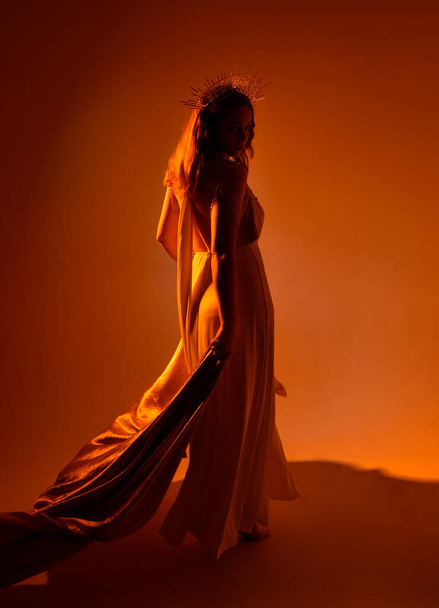 retrato de mujer hermosa cabeza roja con vestido de toga de fantasía de flujo largo con corona halo de oro angelical en el fondo del estudio - Foto, Imagen