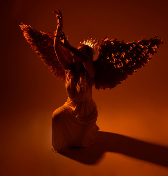портрет красивой рыжеволосой женщины в длинном фэнтези тога платье с ангельской золотой венцом гало на студийном фоне - Фото, изображение