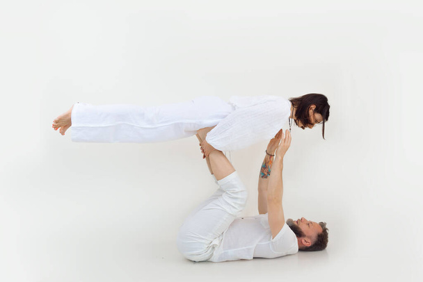 Athletic and sportive family of man and woman practicing yoga, pilates and fitness, husband holding wife in the air on his legs. Healthy lifestyle and family meditation on white studio background - Fotoğraf, Görsel