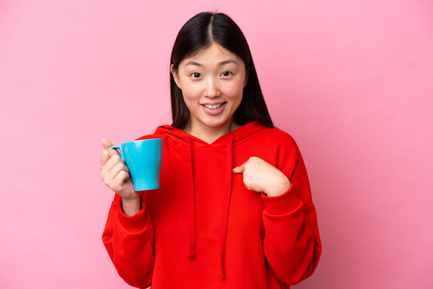 Молодая китаянка держит чашку кофе на розовом фоне с неожиданным выражением лица - Фото, изображение