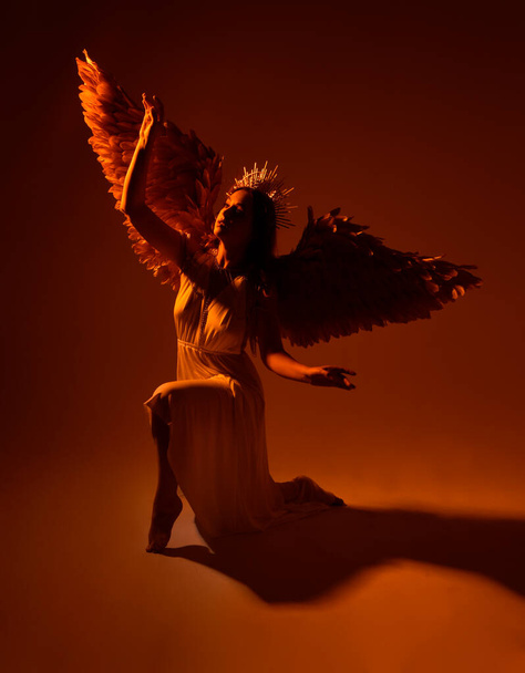 ritratto di bella donna testa rossa che indossa lungo fluente fantasia toga abito con angelico aureola corona d'oro su sfondo studio - Foto, immagini