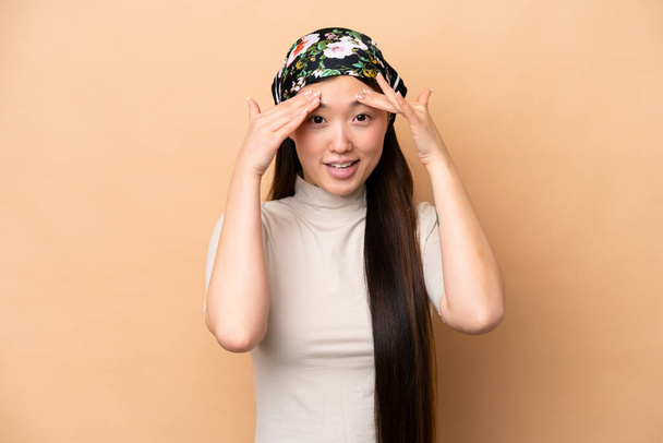 Young Chinese woman isolated on beige background with surprise expression - 写真・画像