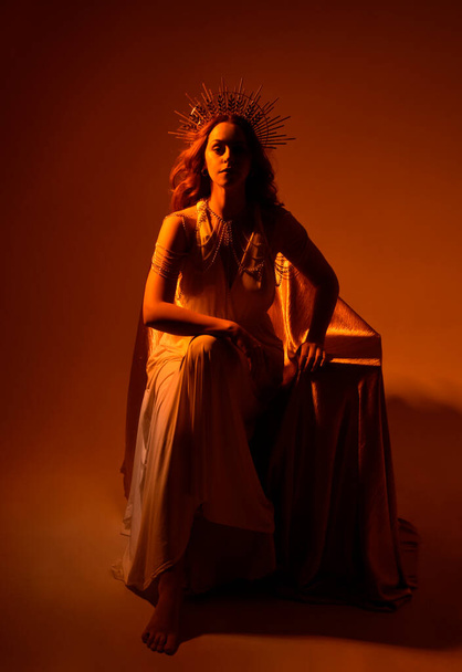 muotokuva kaunis punainen pää nainen yllään pitkä virtaava fantasia tooga puku enkelimäinen kultainen halo kruunu studiolla taustalla - Valokuva, kuva