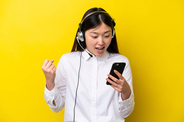 Telemarketer Chińska kobieta pracuje z słuchawki izolowane na żółtym tle zaskoczony i wysyłanie wiadomości - Zdjęcie, obraz