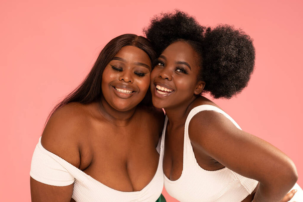 Two beautiful happy women with amazing toothy smiles posing together on pink pastel studio background. Real people emotions. Friendship and happiness - Φωτογραφία, εικόνα