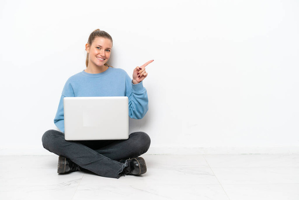 Giovane donna con un computer portatile seduto sul pavimento che punta il dito verso il lato
 - Foto, immagini