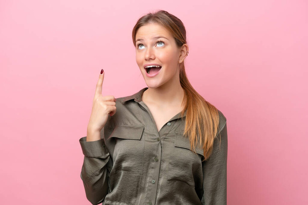 Young caucasian woman isolated on pink background pointing up and surprised - 写真・画像