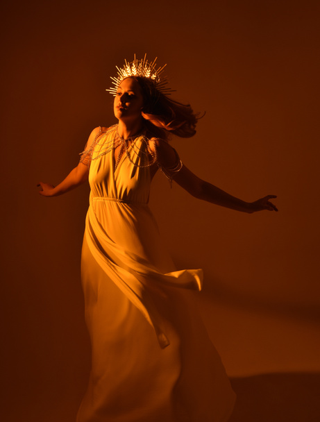 portret pięknej rudej kobiety w długiej, płynącej fantazyjnej todze z anielską złotą koroną aureoli na tle studia - Zdjęcie, obraz