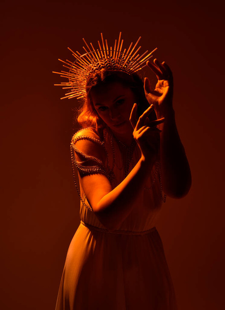 портрет красивой рыжеволосой женщины в длинном фэнтези тога платье с ангельской золотой венцом гало на студийном фоне - Фото, изображение
