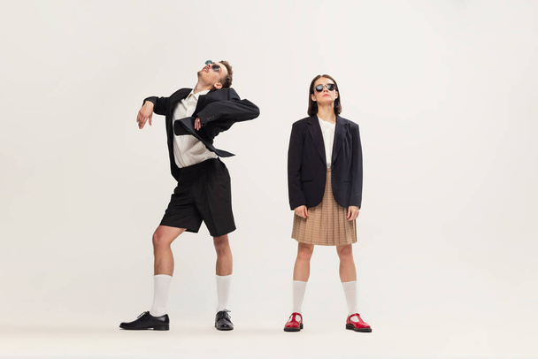 Portrait of stylish young couple, man and woman in retro suit posing isolated over grey studio background. Weird dance. Concept of retro fashion, art photography, style, queer, beauty - 写真・画像