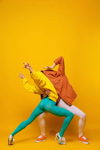 Ritratto creativo colorato di uomo e donna in abiti luminosi con volti nascosti in posa isolata su sfondo giallo. Ballando. Concetto di moda retrò, fotografia d'arte, stile, queer, bellezza - Foto, immagini