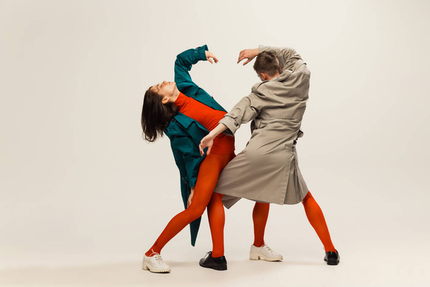 Portrait of stylish man and woman in coats and tights posing isolated over grey studio background. Weirdness, expression. Concept of retro fashion, art photography, style, queer, beauty, party - Photo, Image