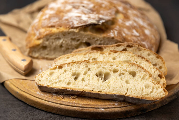 Weißes Scheibenbrot und Messer. Ein Laib Brot, wobei die erste Hälfte bereits geschnitten ist. Drei Scheiben geschnittenes Brot - Foto, Bild