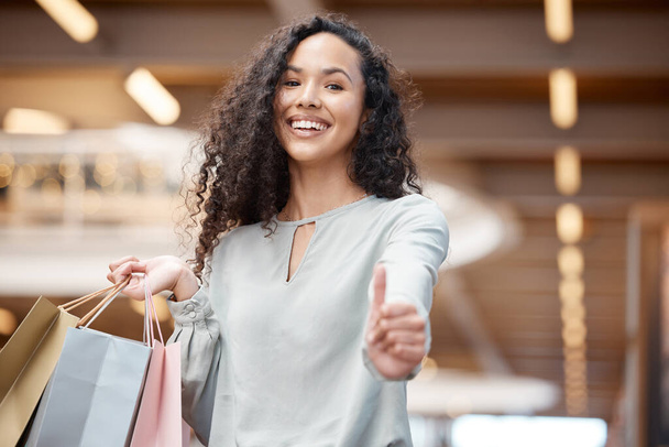 Portrait beautiful mixed race woman giving thumbs up and standing in a mall while shopping. Young hispanic woman carrying bags, spending money, looking for sales and enjoying her retail therapy. - 写真・画像
