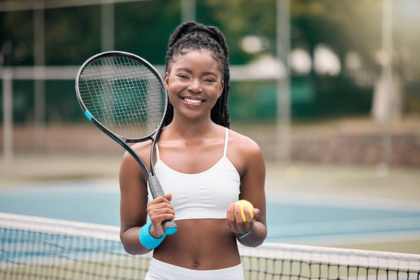 Un tenista sonriente sosteniendo una pelota. Chica afroamericana lista para su partido de tenis en el club. Mujer joven sosteniendo su pelota de tenis y raqueta en la cancha. Chica listo para la práctica de tenis. - Foto, imagen