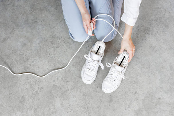 Woman inserting electric dryer into her white sneakers, close-up on shoes. Concept of household technologies and smart gadgets - Fotografie, Obrázek