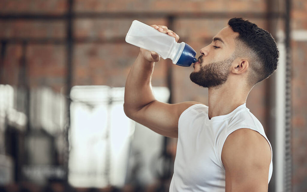Man taking a break from exercise to hydrate.Young man drinking water from a bottle during exercise. Active fit man drinking water during a workout. Bodybuilder taking a break from exercise. - Foto, imagen