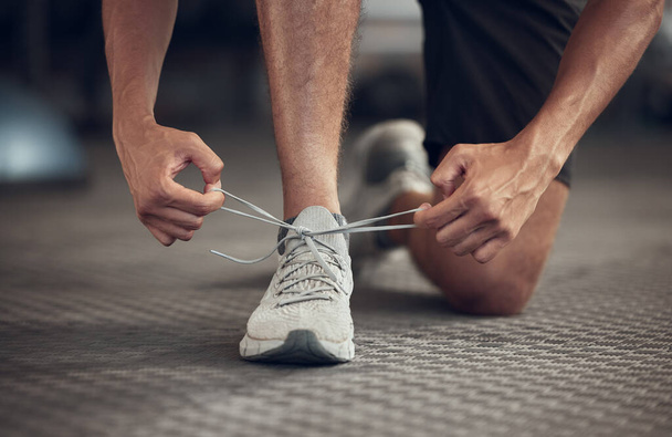 Closeup of athlete tying his shoelaces in the gym. Hands of fit man getting ready with his gym shoes. Bodybuilder ready to workout. Fit athlete tying the laces of a sport sneaker. - Zdjęcie, obraz