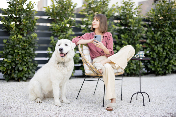 Young woman sitting relaxed with her huge white adorable dog, spending time together at backyard. Friendship with pet and happy leisure time outdoors concept - Photo, Image