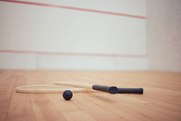 Group of squash equipment and gear on wooden floor in empty court in sports centre with copyspace. Two rackets and ball arranged in sporty arena with nobody before championship game and competition. - Фото, изображение