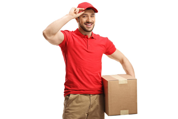 Delivery man with a box smiling and greeting with cap isolated on white background - Foto, afbeelding