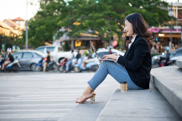Asiatische Geschäftsfrau mit Laptop arbeitet draußen und schaut auf Bildschirme im Geschäftsviertel, professionelle Frauen sitzen draußen - Foto, Bild