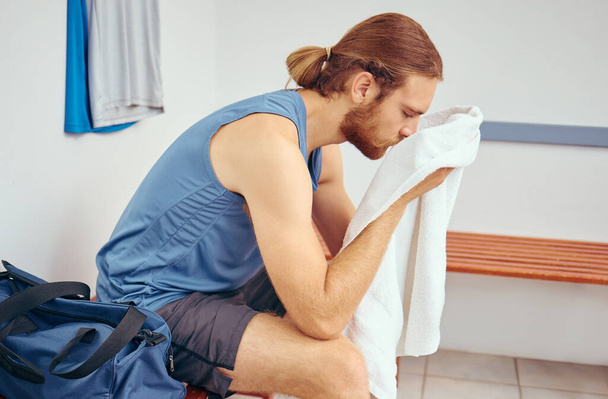 Caucasian player wiping his face with a towel. Tired young player wiping his face after a squash match. Professional athlete taking a break from his squash match to rest in a gym locker room. - Foto, Bild