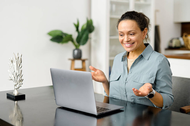 Freelancer feminino inteligente positivo sentado à mesa com laptop, estudando a partir de webinar on-line ou um curso em casa, chamada de vídeo e conversando - Foto, Imagem